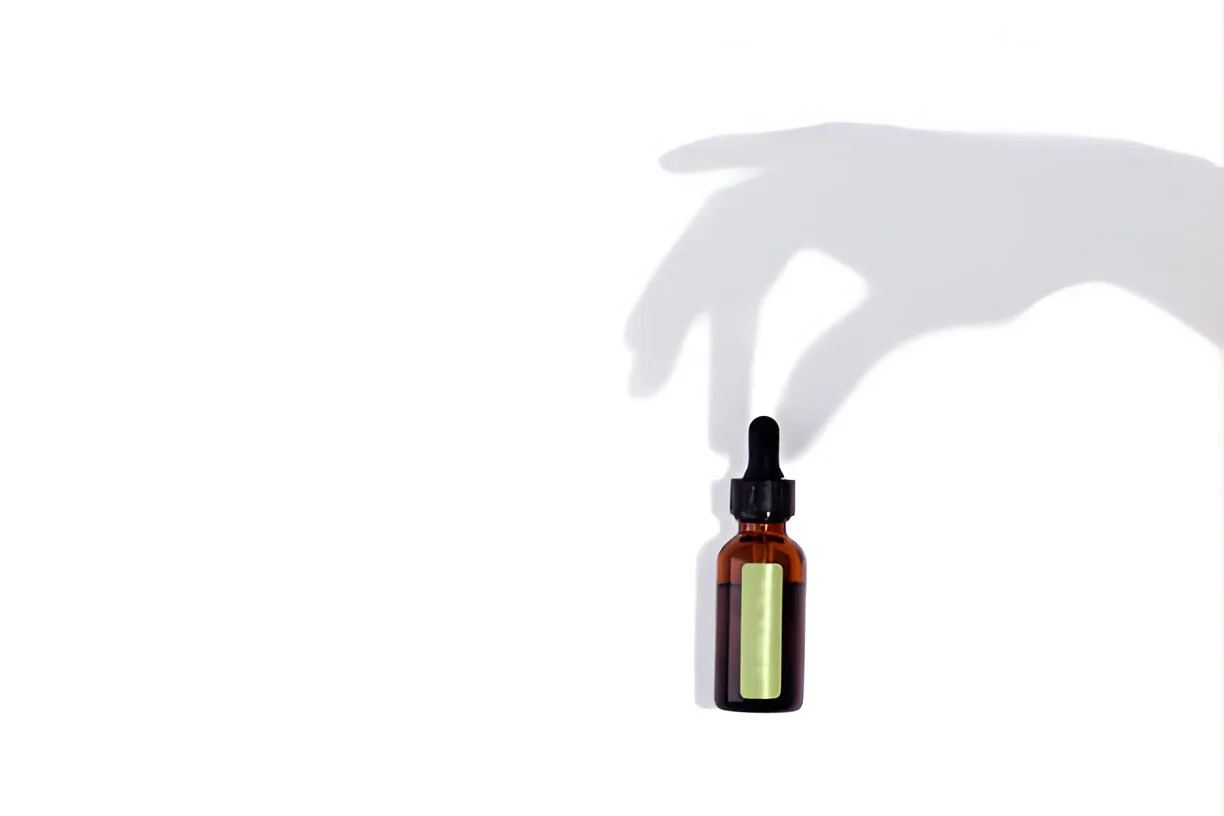 Amber glass bottle of oral tirzepatide drops with a shadow of a hand reaching for it on a white background, symbolizing easy access and use.