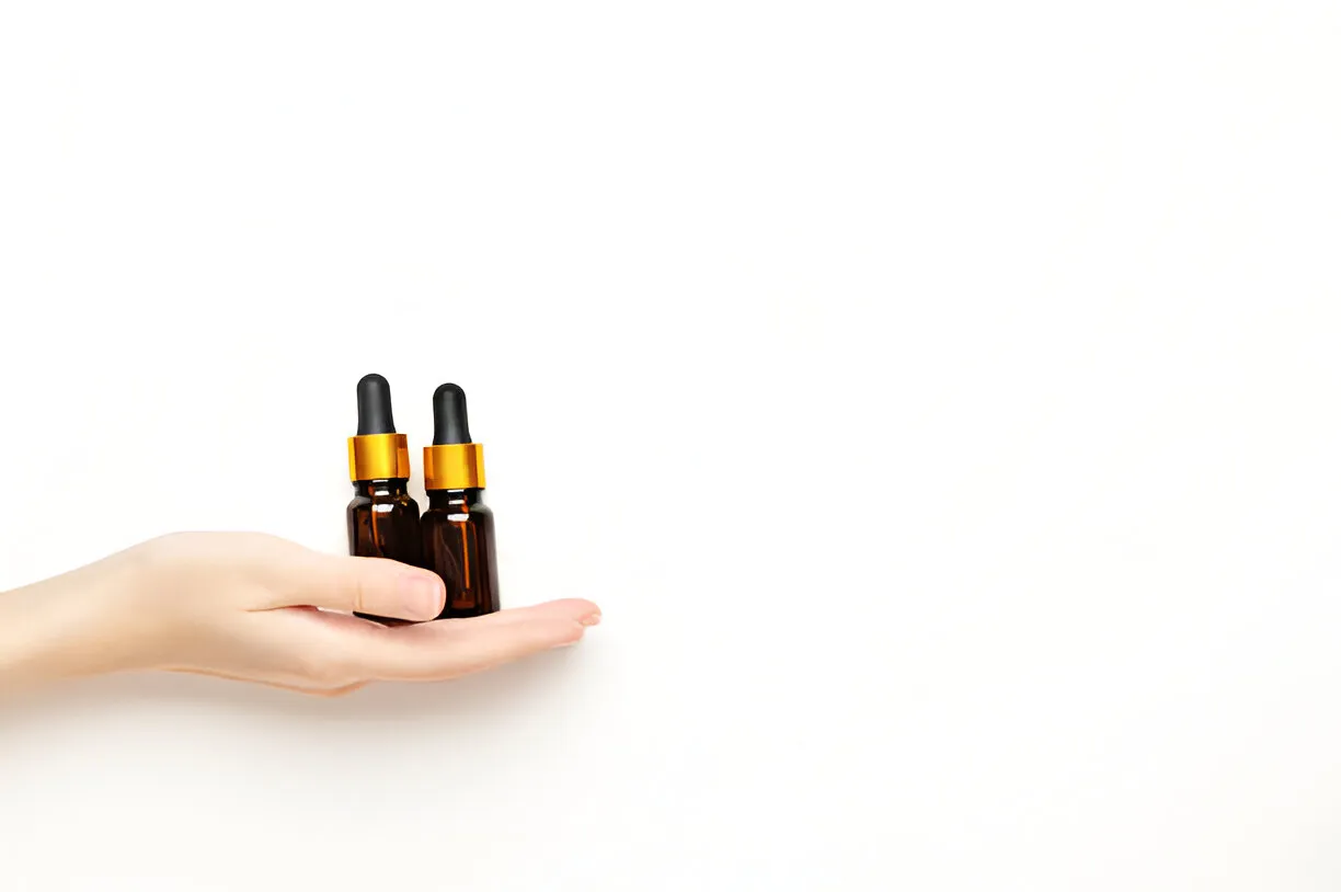 Two amber bottles of oral tirzepatide drops with gold caps held in a human hand on a white background, representing modern weight loss medication.