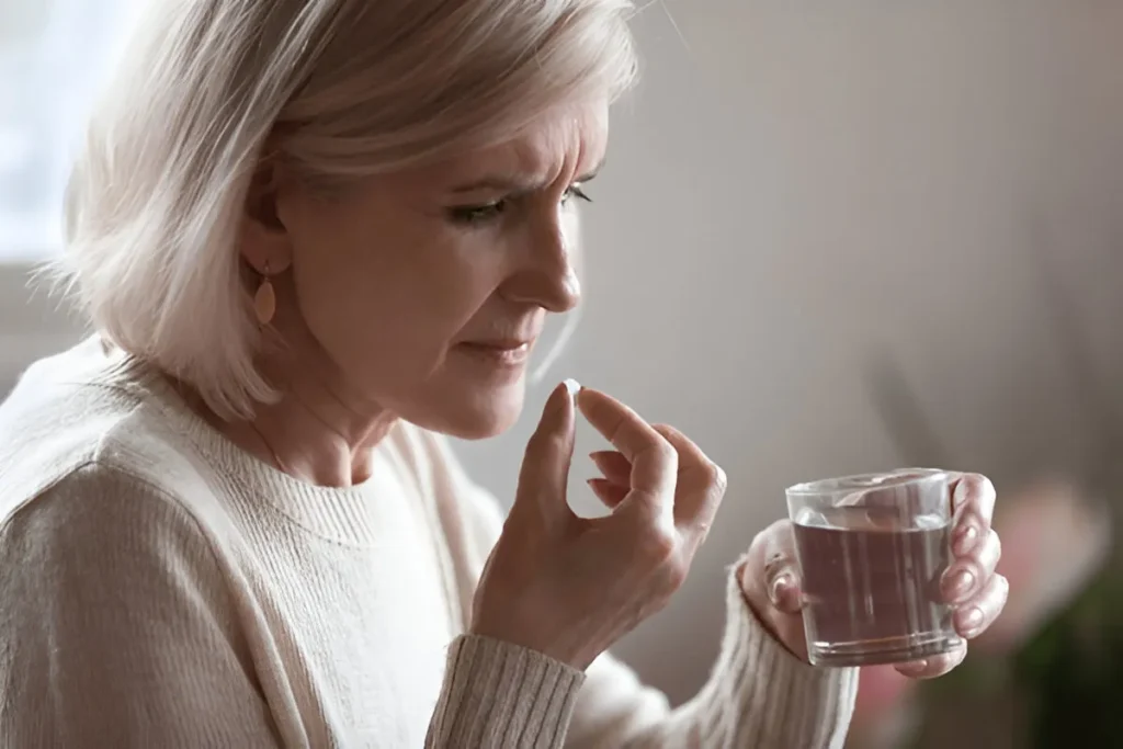 Senior woman holding a pill and glass of water – oral medication or supplement intake for health and wellness