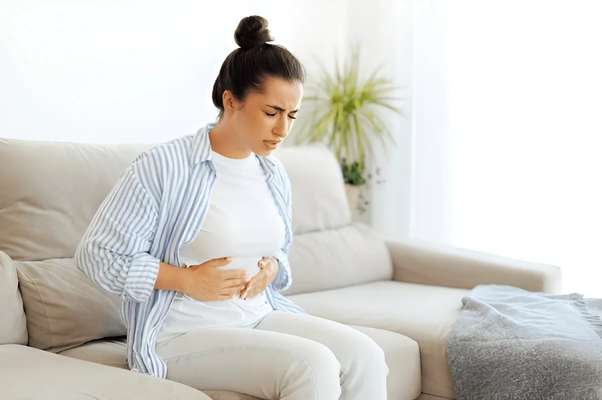 Young woman experiencing stomach pain on couch – side effects of oral tirzepatide may include nausea or gastrointestinal discomfort