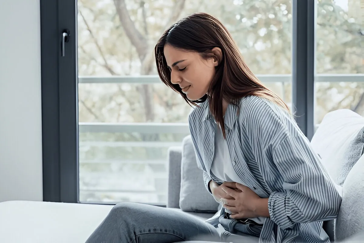 Young woman with abdominal discomfort on couch – side effects of oral tirzepatide may include nausea, cramping, or stomach pain.