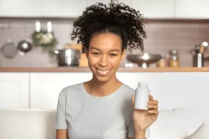 Smiling woman holding a supplement bottle at home, representing microdosing for wellness.